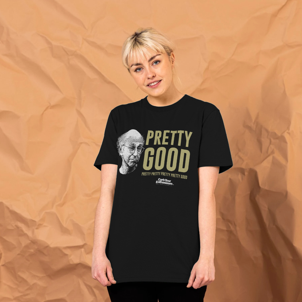 A woman standing in front of a brown paper backdrop, wearing a black crew neck t-shirt with the text 'PRETTY GOOD' and a graphic print in gold.