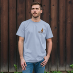 Man wearing a light blue t-shirt with a logo, standing against a wooden wall.