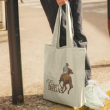 Tote bag with a horse and rider design held by a person on a sidewalk.