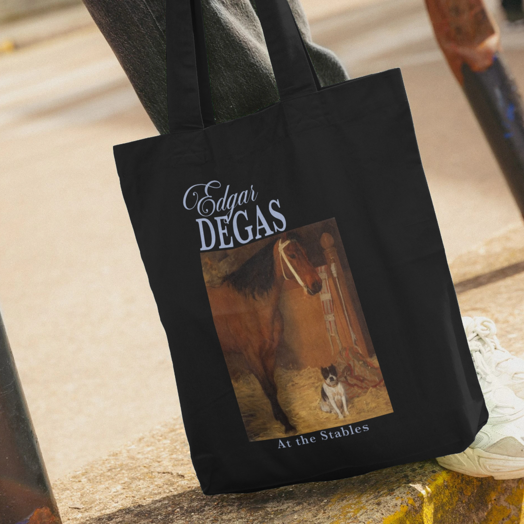 Black tote bag with artwork of a horse and text 'Edgar Degas At the Stables' held by a person.