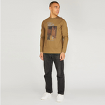 Man wearing a brown long-sleeve shirt with a graphic design and dark jeans on a white background