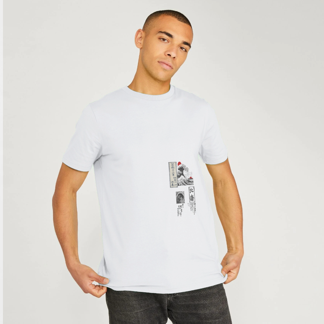 A man wearing a white crew-neck t-shirt with a small graphic print on the left chest, paired with dark gray jeans, against a light gray studio background.